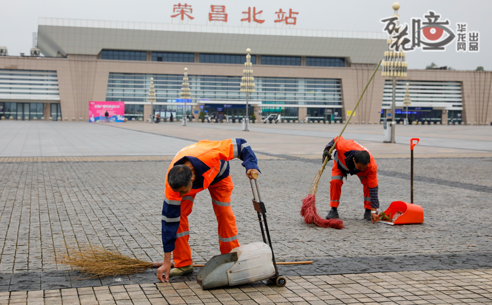 榮昌北站站前廣場上，環衛工人手持掃帚，為機器普掃后的地面進行精細保潔。他們專注于路沿的邊角，一如往昔。老師傅的經驗與新科技的效率在此刻完美交融，活干得又好又快，為往來的人們留下一片潔凈。