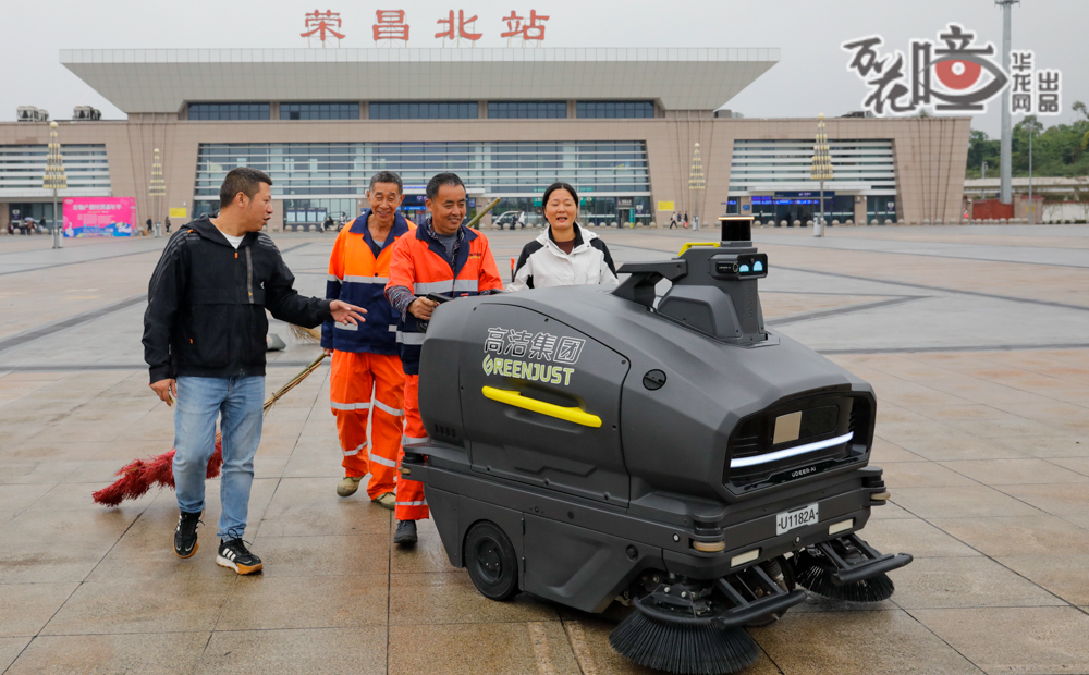 榮昌北站，蒙蒙細雨里，身穿橙色工作服的環衛工人梁甫輝格外耀眼，他正與“新搭檔”——一輛自動駕駛清掃車，進行著溫柔的對話。他那雙刻畫著歲月年輪的手，如今正學習著新的語言：雙手輕捏按鈕是前進，左手按下便是向左轉。這個聰明的新伙伴雖能自主清掃廣場，但有時候還是需要老師傅來幫忙。