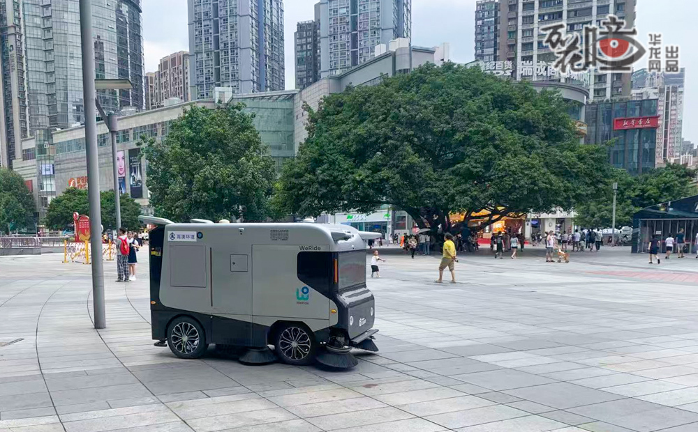  在九龍坡楊家坪商圈廣場上，一臺無人掃路機正沉穩有序地穿行。結合智能監控和調度算法，使它靈巧地避讓往來行人，同時精準吸拾路面垃圾。它這片繁華商圈中穿梭自如，既保持了市容整潔，又成為現代城市管理中一道獨特的科技風景線。