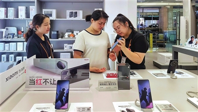 重百梁平商場(chǎng)一樓的小米之家梁平店，工作人員在向市民文國(guó)花（中）介紹手機(jī)性能及以舊換新相關(guān)政策。